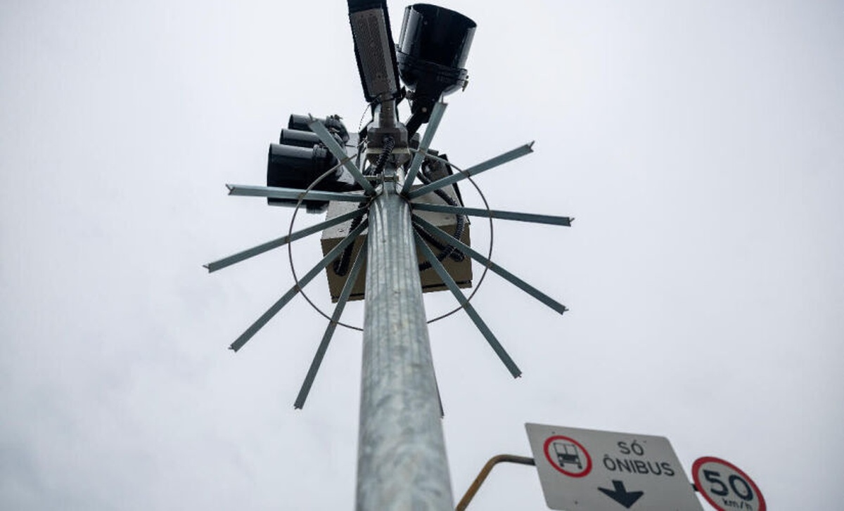 Dispositivo de proteção metálica instalado em radar de trânsito em São Paulo, visto de baixo, destacando tecnologia contra furtos e sinalização viária.