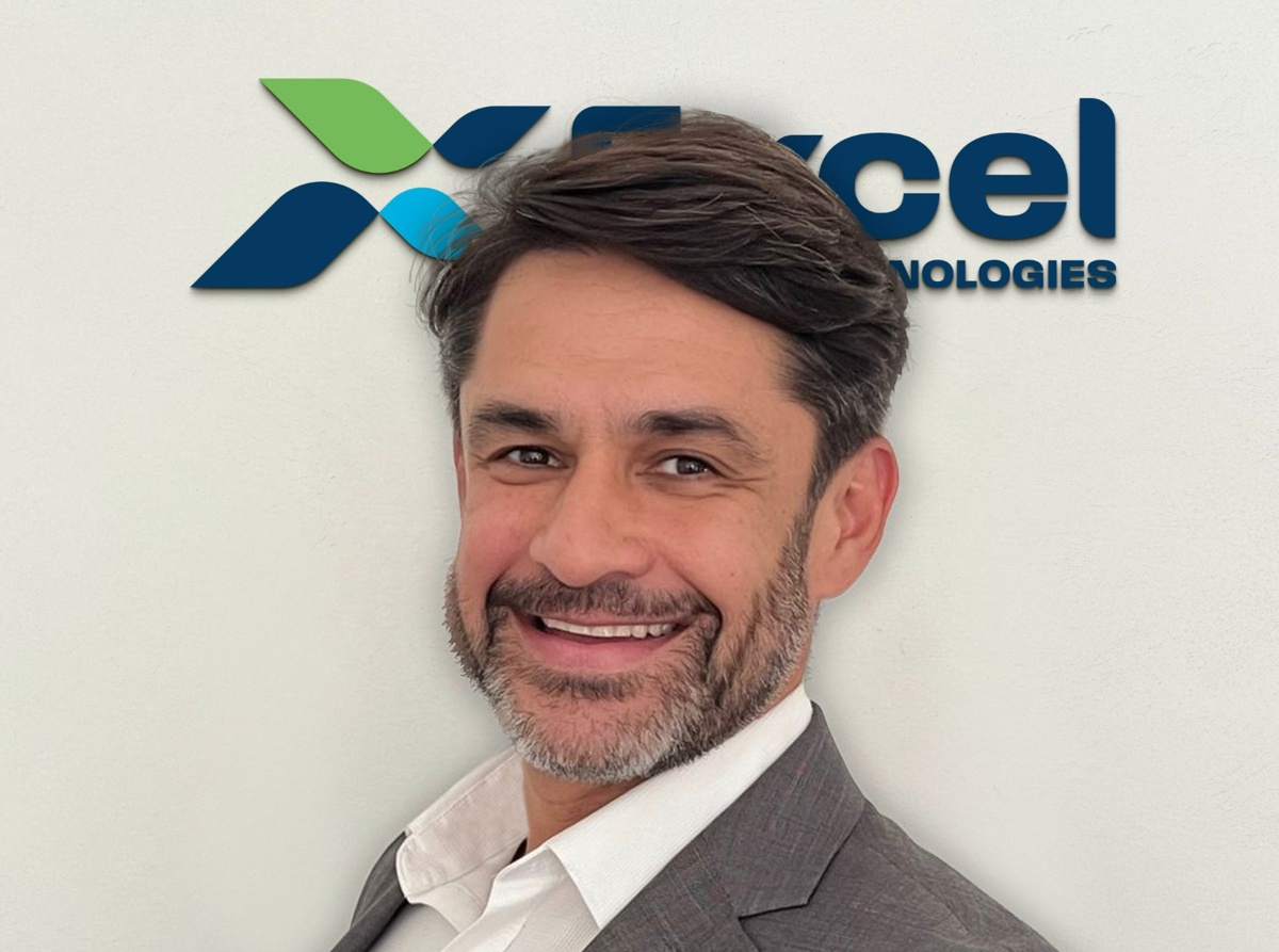 Executivo da Excel Technologies sorrindo diante da logomarca da empresa em fundo branco