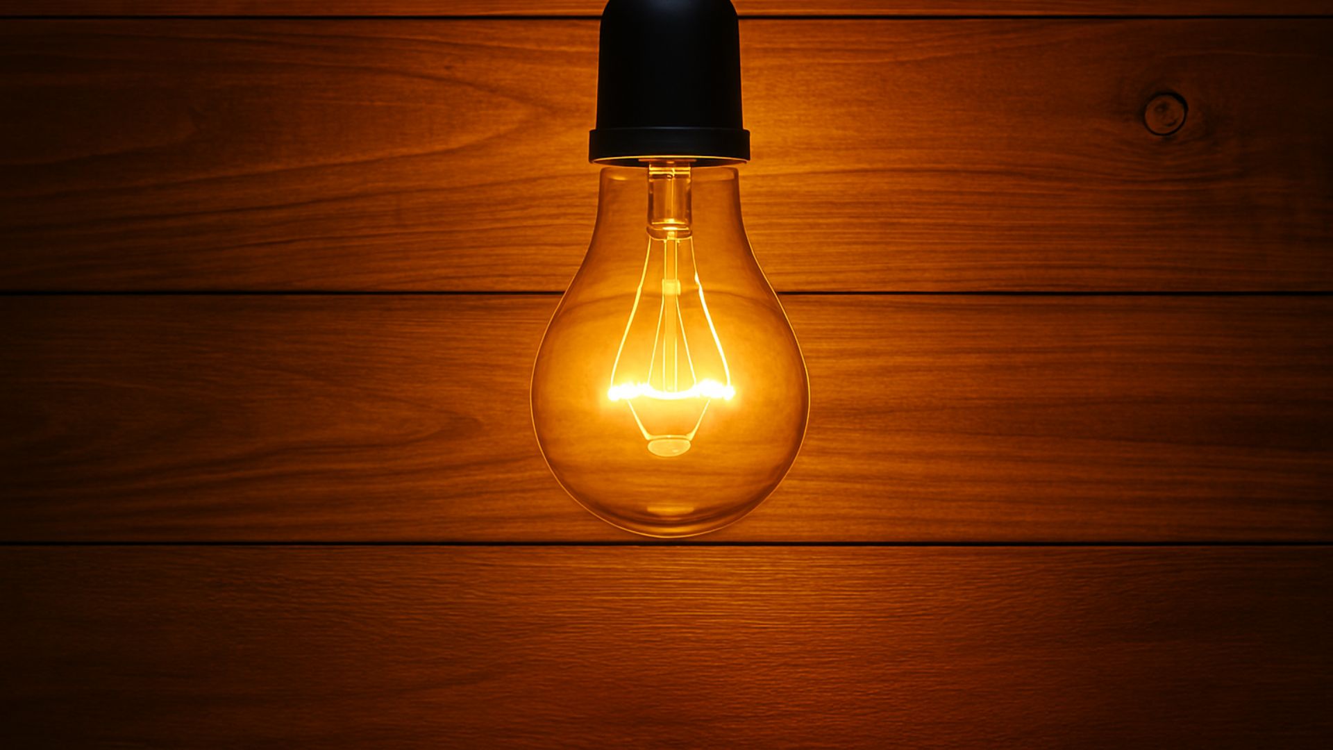 Lâmpada incandescente acesa pendurada ao centro contra fundo de madeira, emitindo luz quente e suave