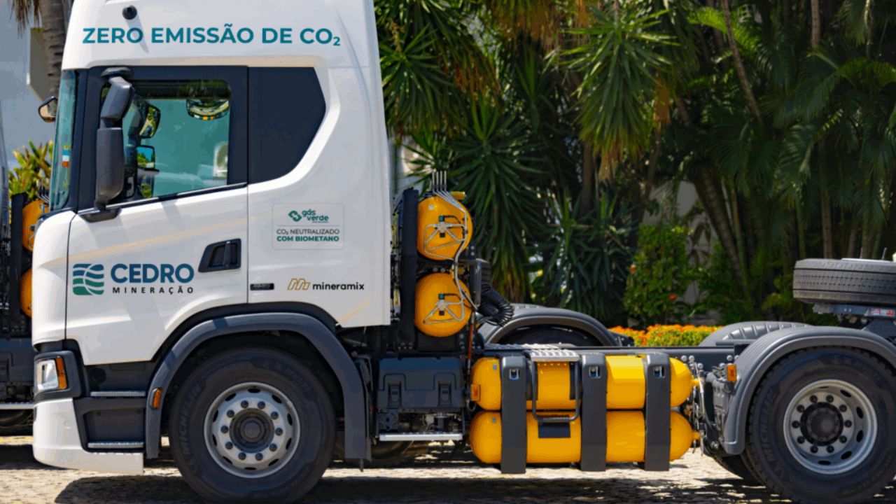Caminhão da Cedro Mineração movido a GNV com tanques amarelos visíveis e mensagem “Zero Emissão de CO₂”, estacionado em ambiente arborizado.