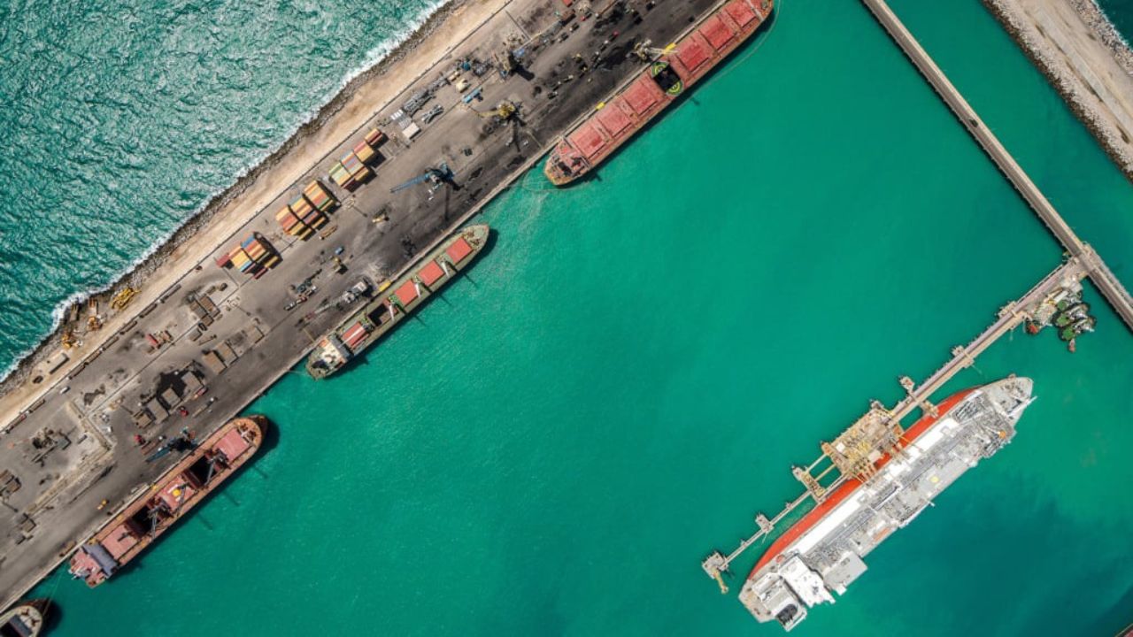 Vista aérea do Porto do Pecém, com navios atracados, guindastes e contêineres em operação sobre águas azul-turquesa.