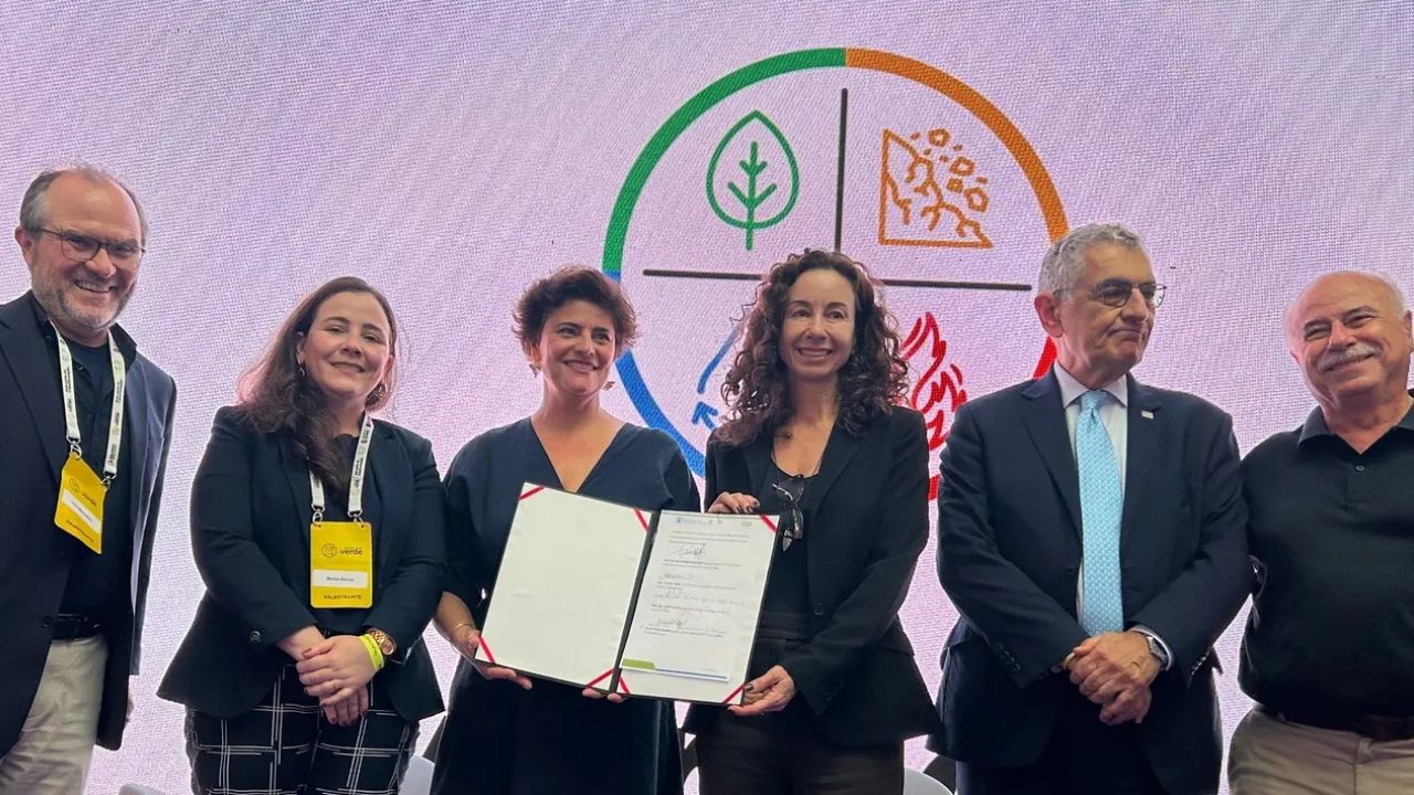 Seis representantes de instituições ambientais e acadêmicas posam diante de um painel temático, enquanto dois deles exibem um documento assinado, simbolizando uma parceria oficial voltada à sustentabilidade.