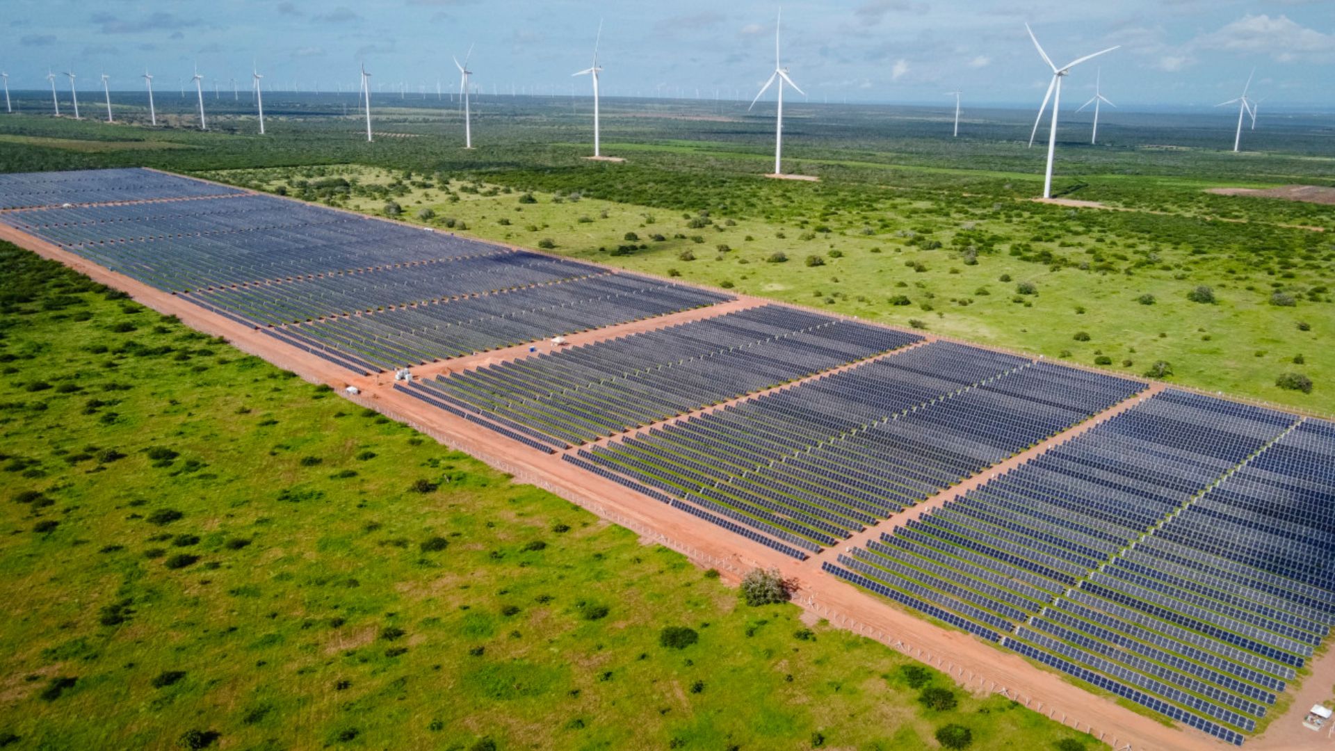 Parque híbrido de energia renovável da Voltalia no Brasil, com usina solar fotovoltaica em primeiro plano e aerogeradores eólicos ao fundo, ilustrando a expansão da capacidade instalada e os desafios de escoamento da geração.